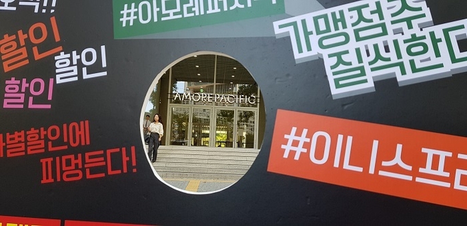 이니스프리 본사에 대한 시정 내용을 담은 피켓 가운데 공간으로 아모레퍼시픽그룹의 CI가 선명하다.