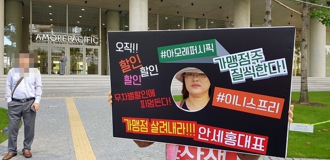 이니스프리 가맹점주가 본사의 갑질과 불공정 거래 행위를 규탄하는 문구가 새겨진 피켓을 들고 본사 앞에서 시위하고 있다.